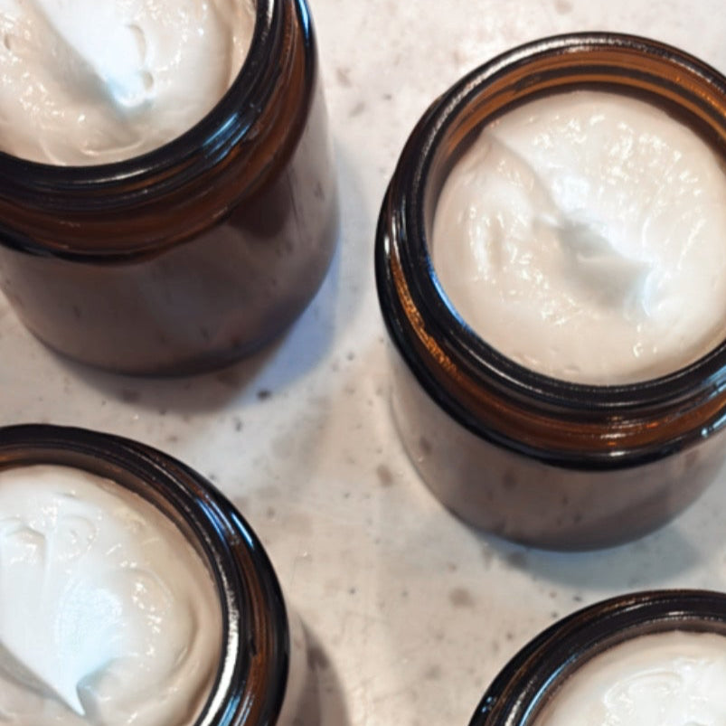 Multiple small jars with a white cream-like substance on a textured surface