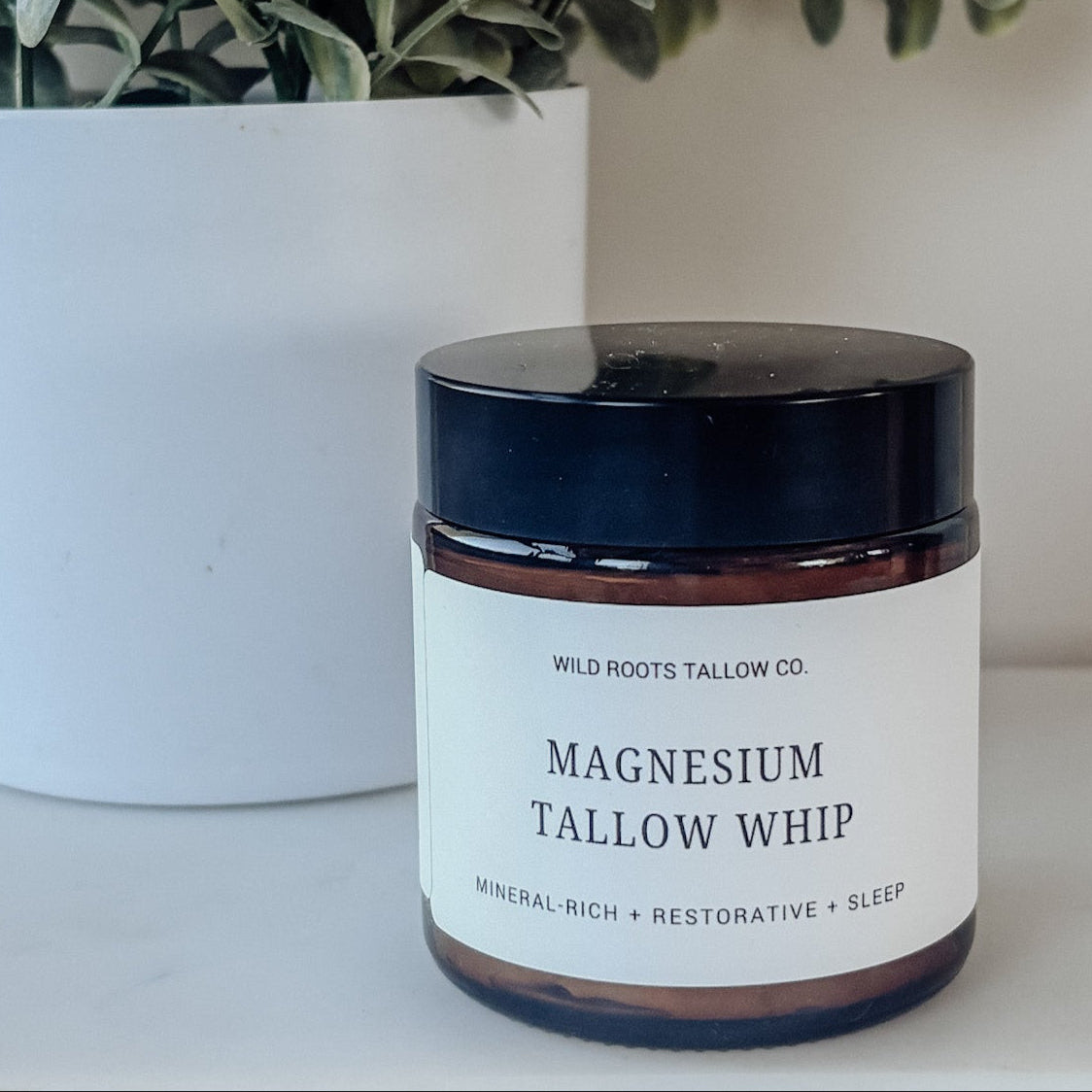 Jar of Magnesium Tallow Whip with a plant in the background on a white surface