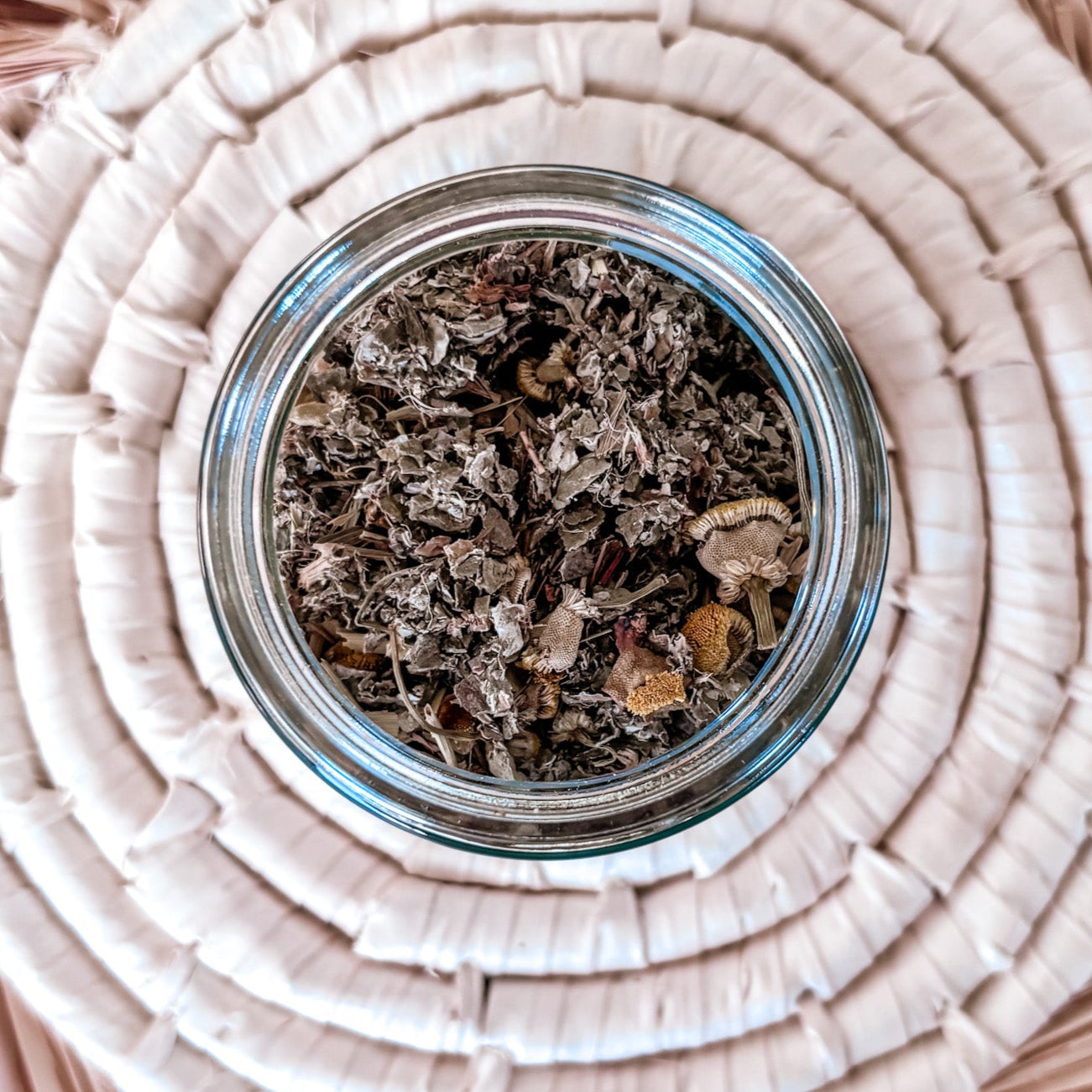 Glass jar with dried herbs on a woven surface