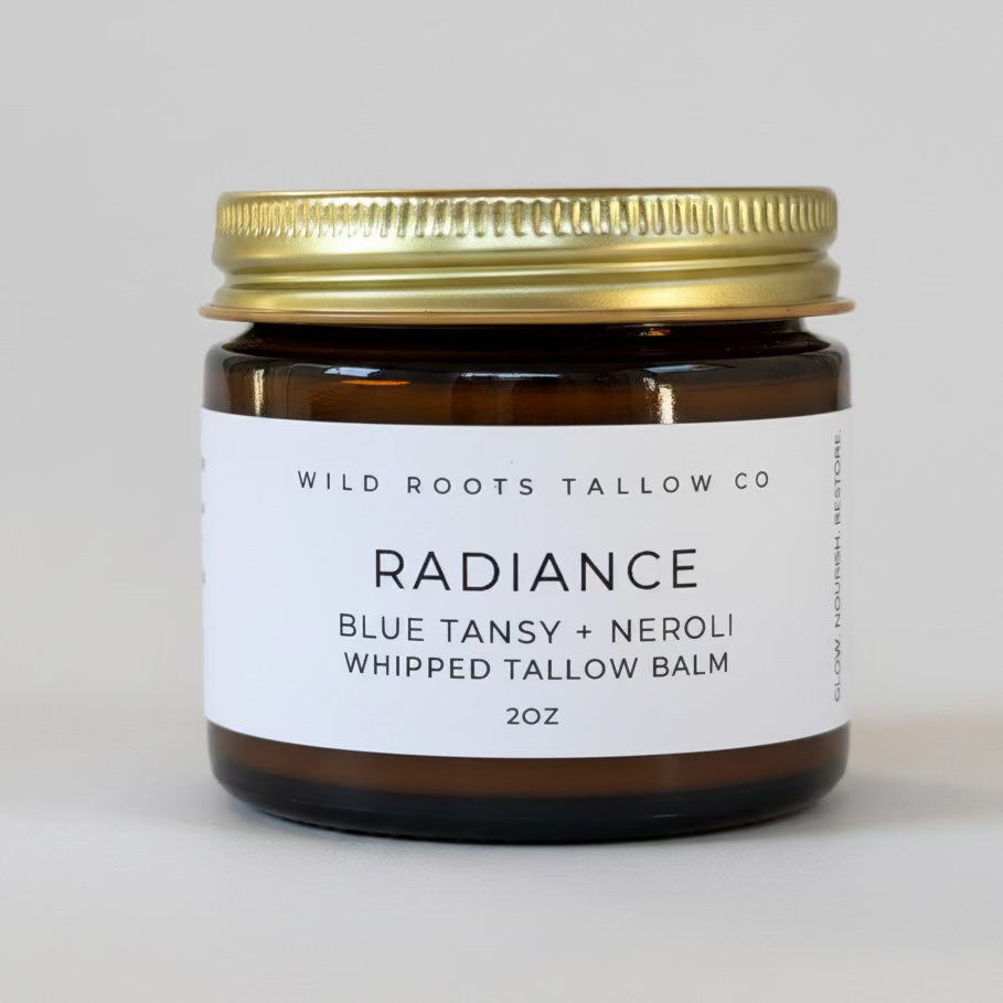 Jar of Wild Roots Tallow Co Radiance balm on a wooden surface with flowers in the background