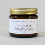 Jar of Wild Roots Tallow Co Radiance balm on a wooden surface with flowers in the background