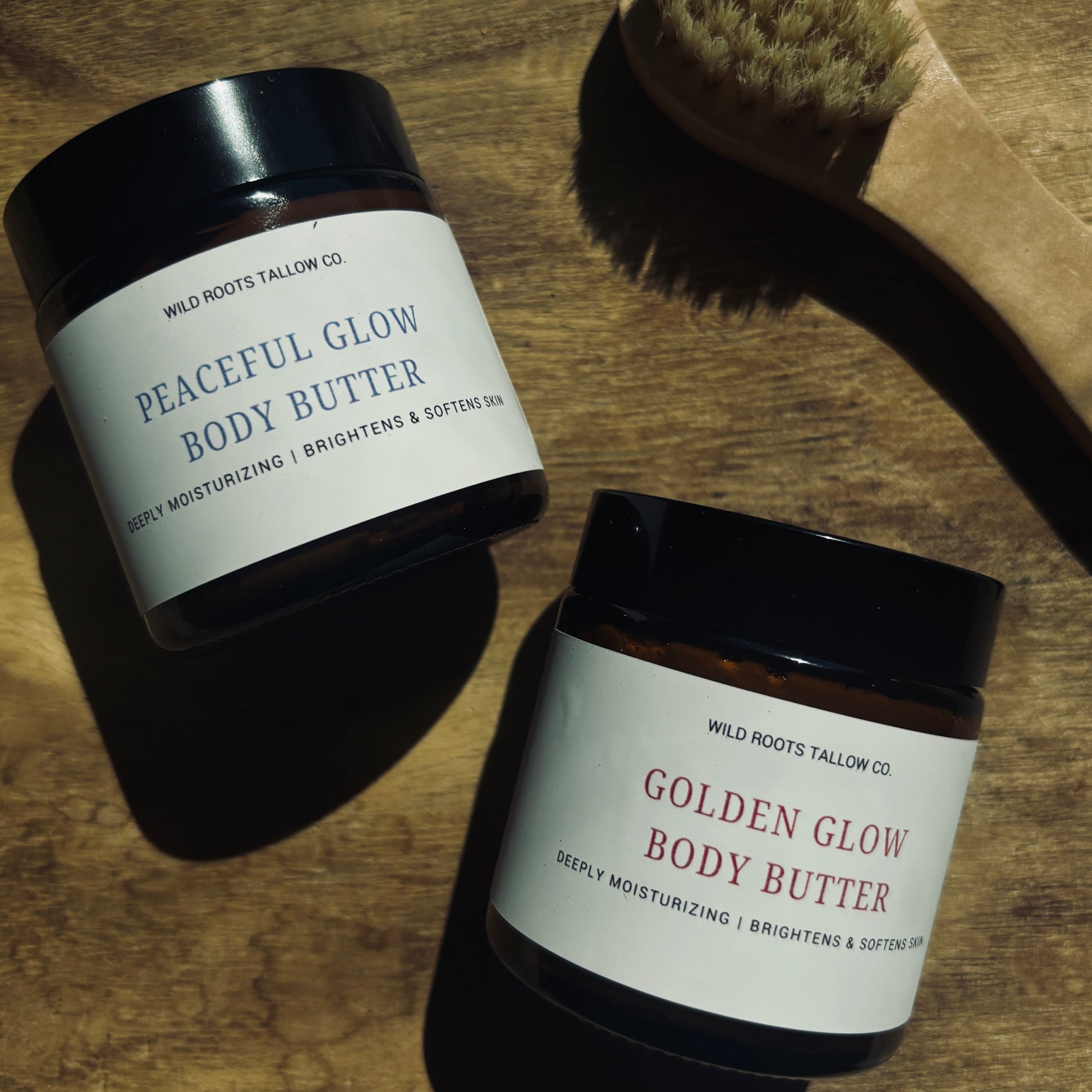 Two jars of body butter labeled 'Peaceful Glow' and 'Golden Glow' on a wooden surface with a brush.