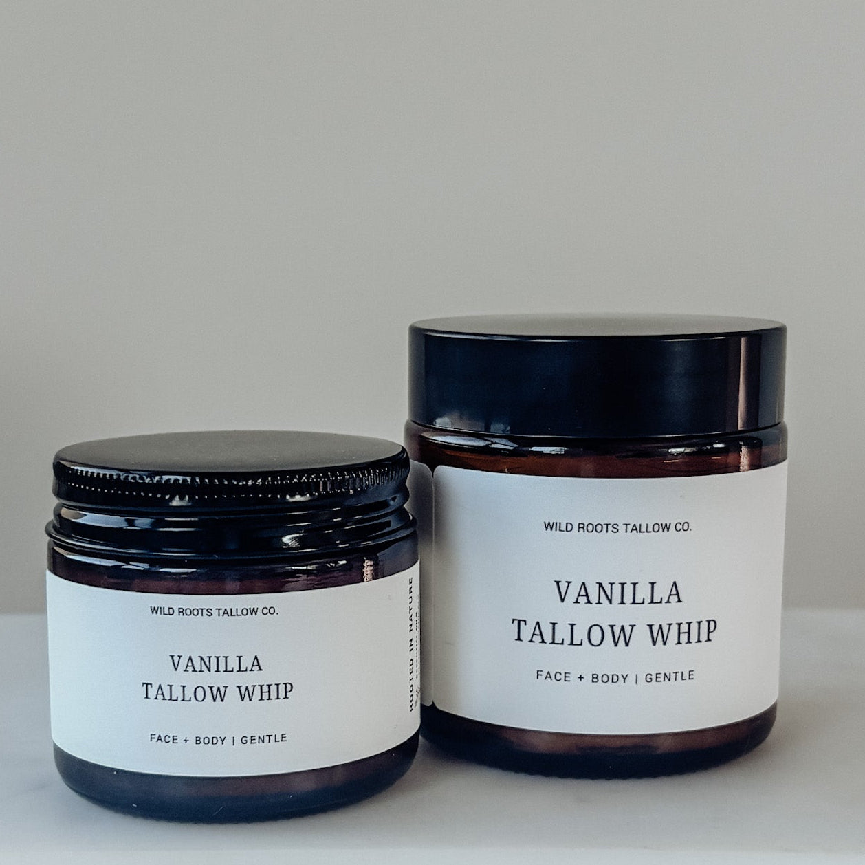 Two jars of Vanilla Tallow Whip on a white surface with a neutral background