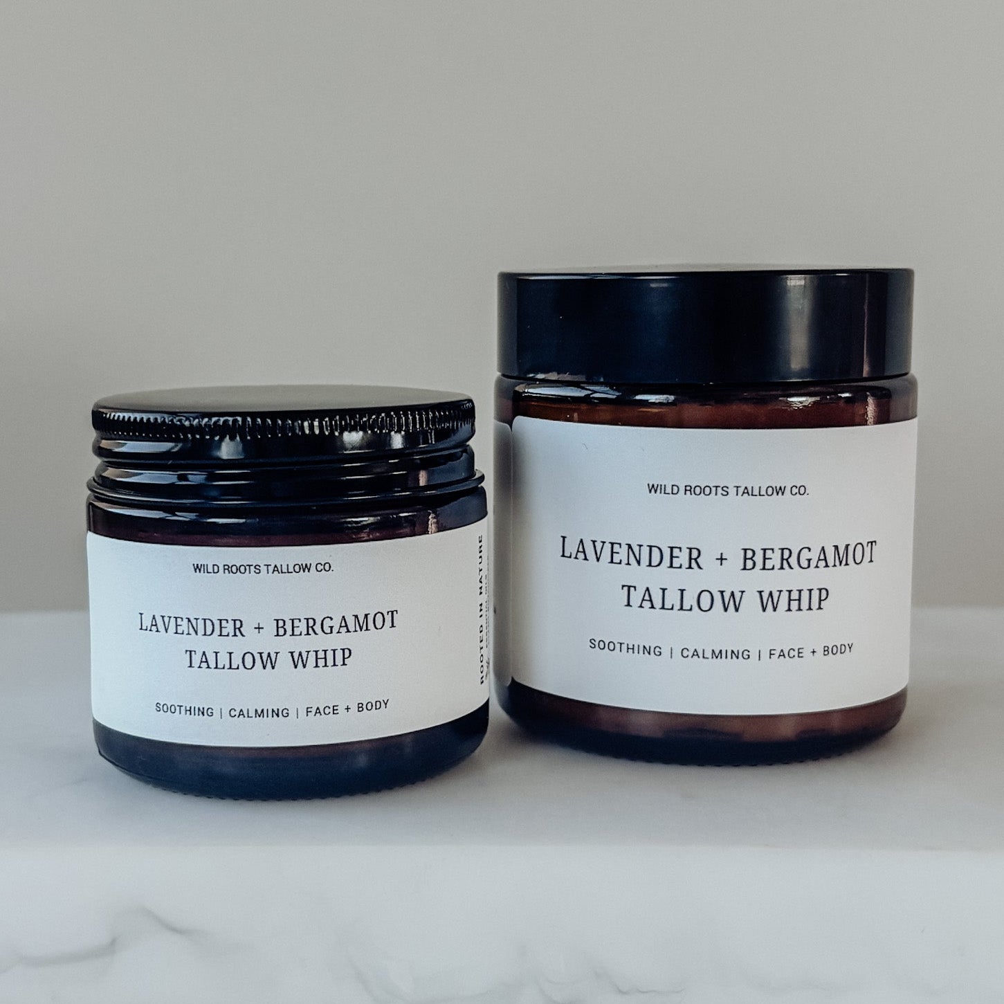 Two jars of lavender bergamot tallow whip on a marble surface with a neutral background