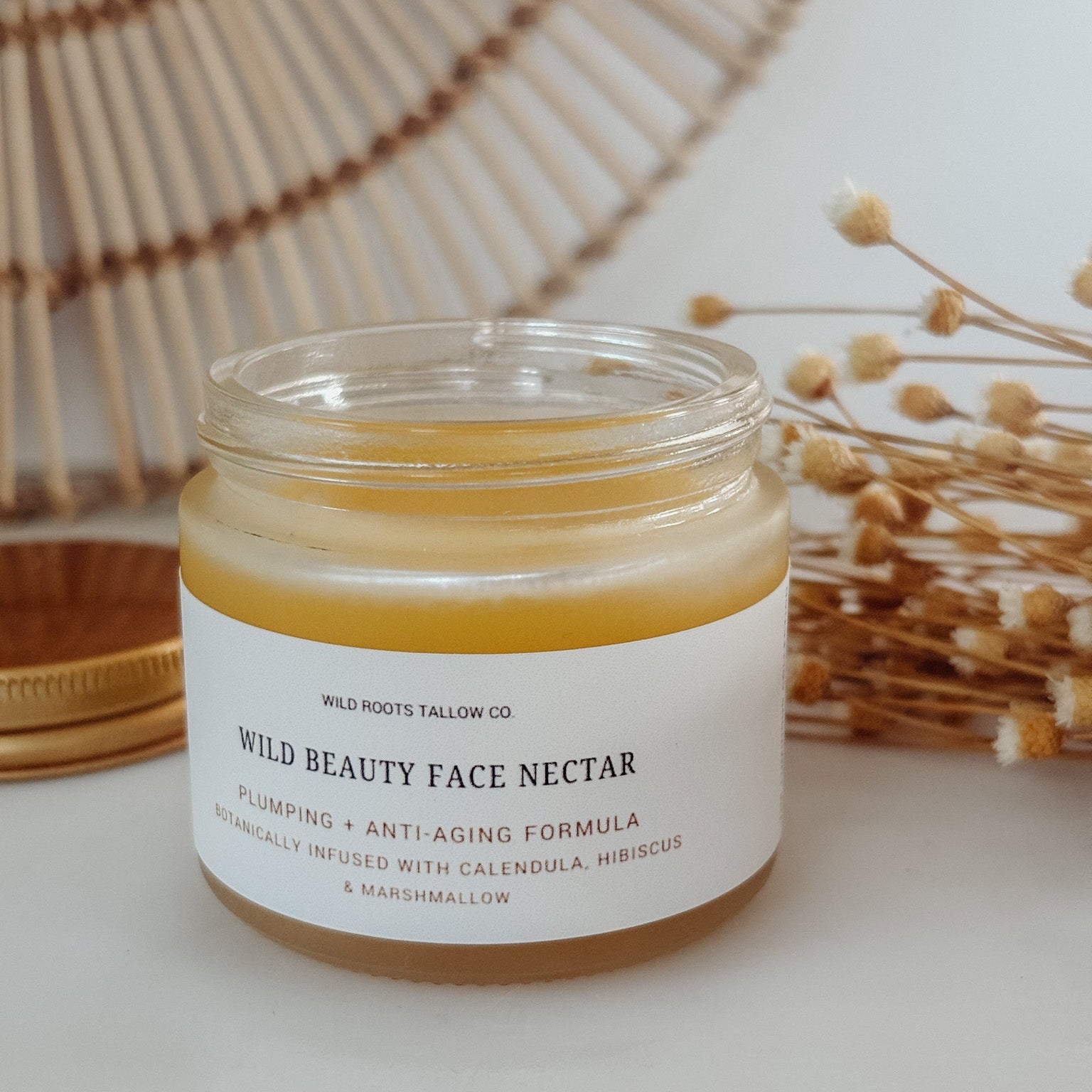 Jar of Wild Beauty Face Nectar on a marble surface with a woven basket and dried flowers in the background.